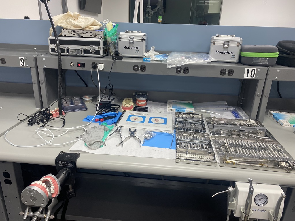 シミュレーションラボの実習台。番号9と10のブースに器具ケースと滅菌カセットが並び、手前の台には歯列模型を固定するマネキンマウントとエアタービンユニットが見える