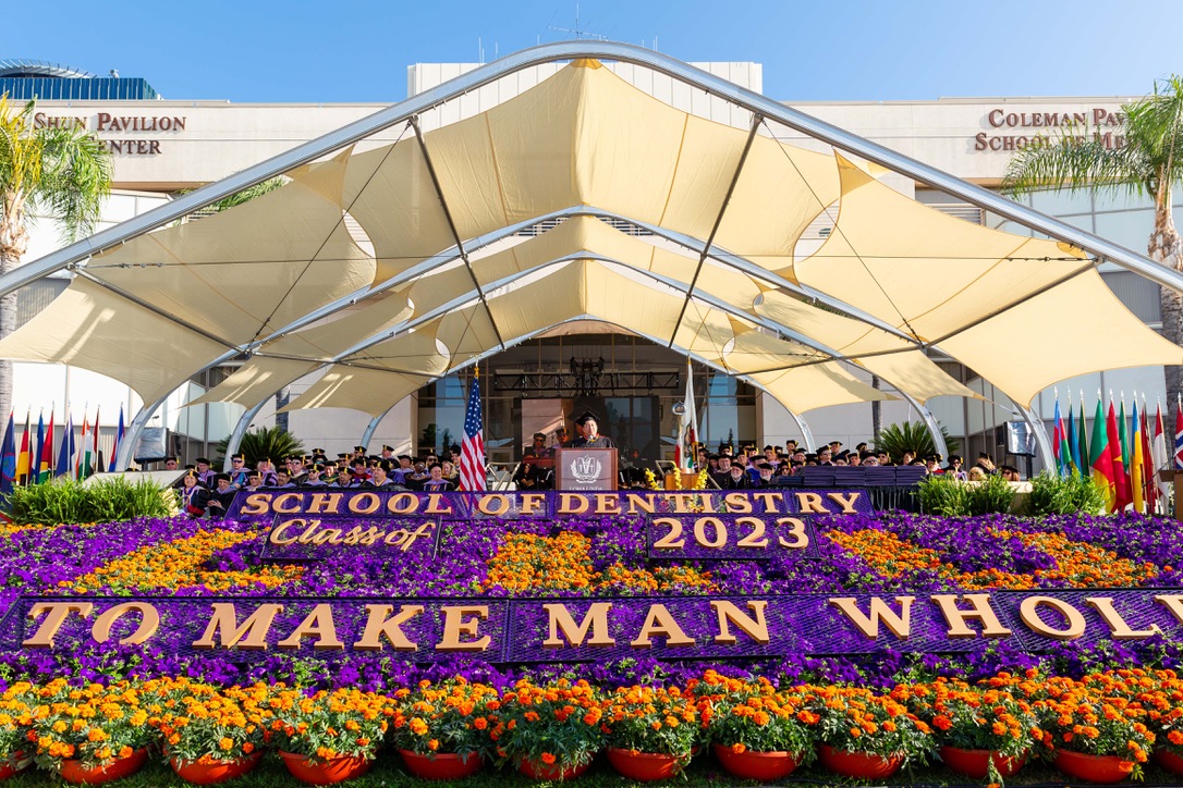 米国 Loma Linda University 歯学部 Class of 2023 の卒業式。壇上に卒業生が並び、花壇に「SCHOOL OF DENTISTRY Class of 2023」「TO MAKE MAN WHOLE」の文字が花で描かれている